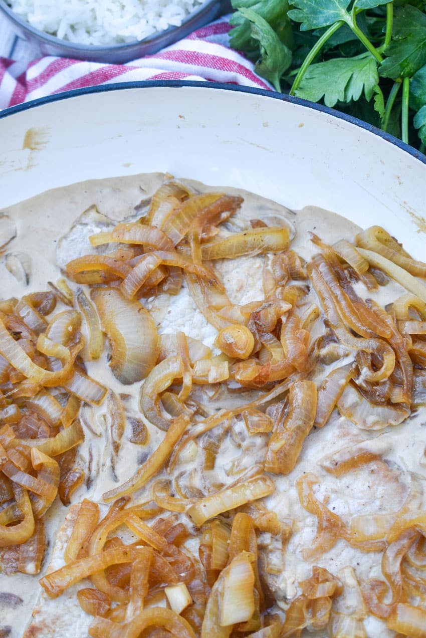 pork chops in cream sauce with caramelized onions in a large enameled cast iron skillet