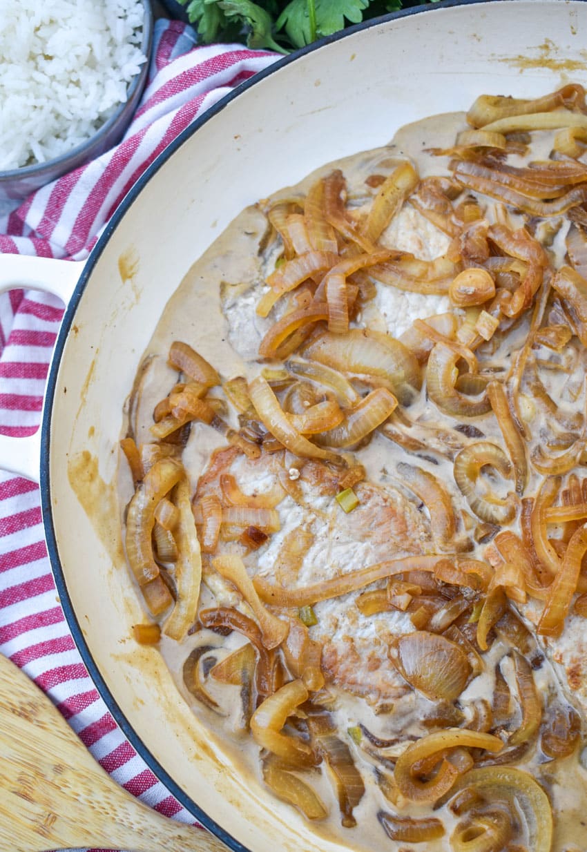 pork chops in cream sauce with caramelized onions in a large enameled cast iron skillet