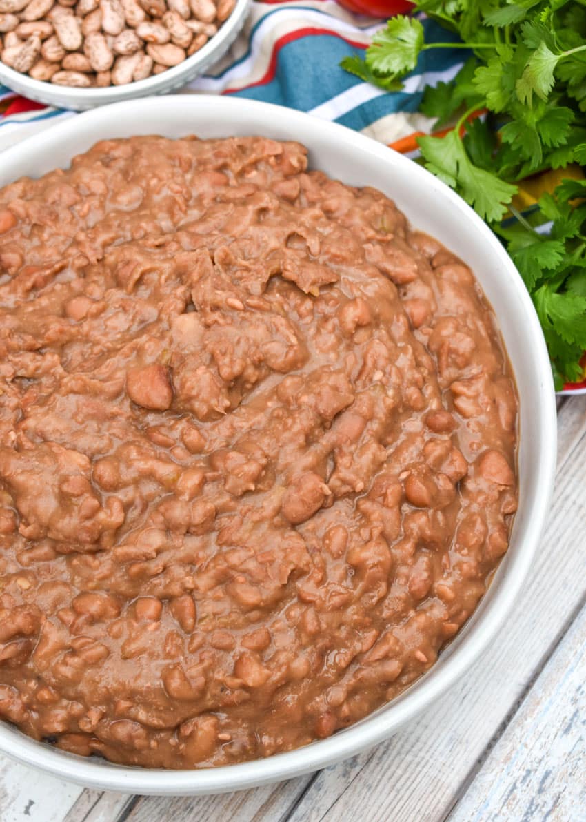 slow cooker refried beans in a shallow white serving bowl