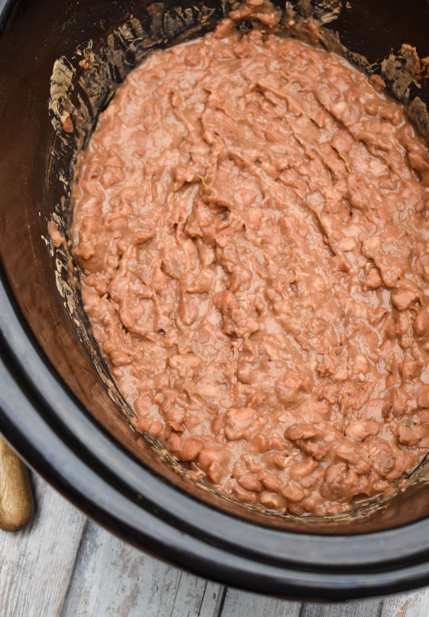 homemade refried beans in the black bowl of a slow cooker
