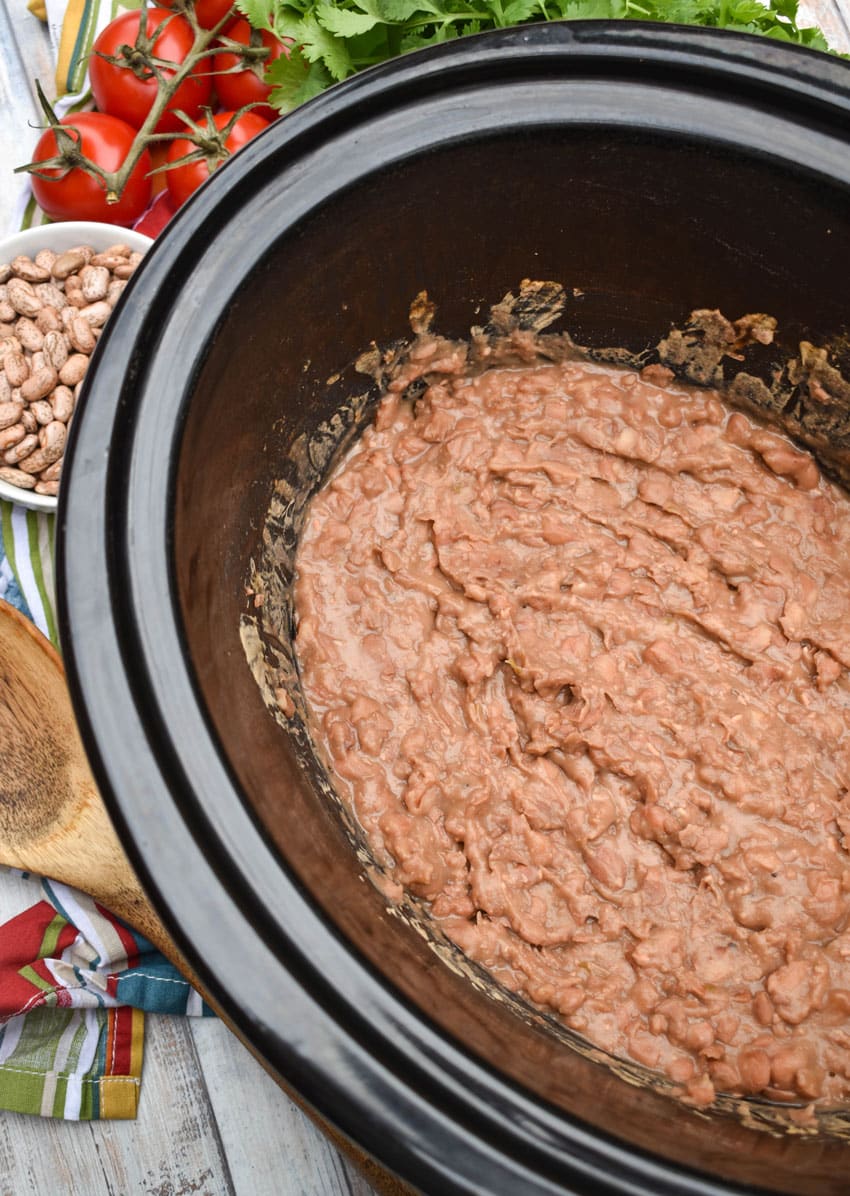 homemade refried beans in the black bowl of a slow cooker