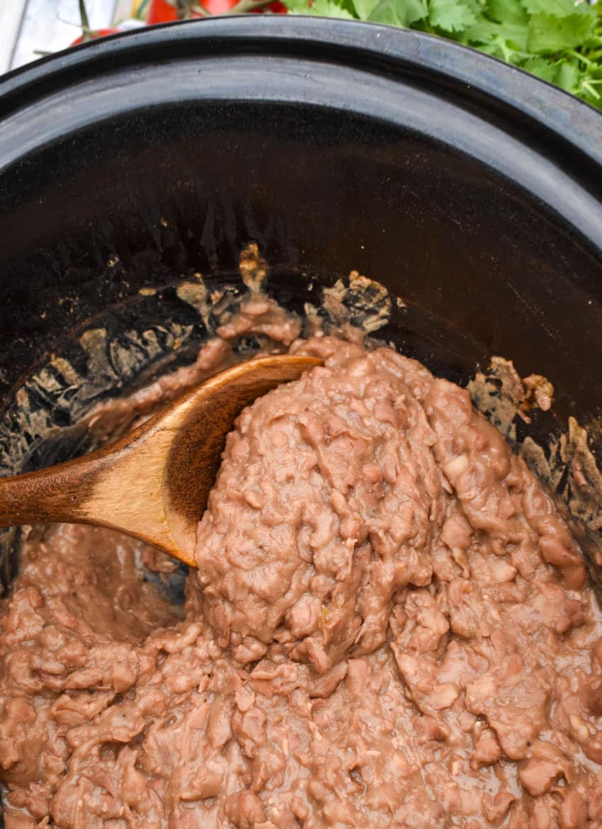 a wooden spoon scooping homemade refried beans out of a black crockpot