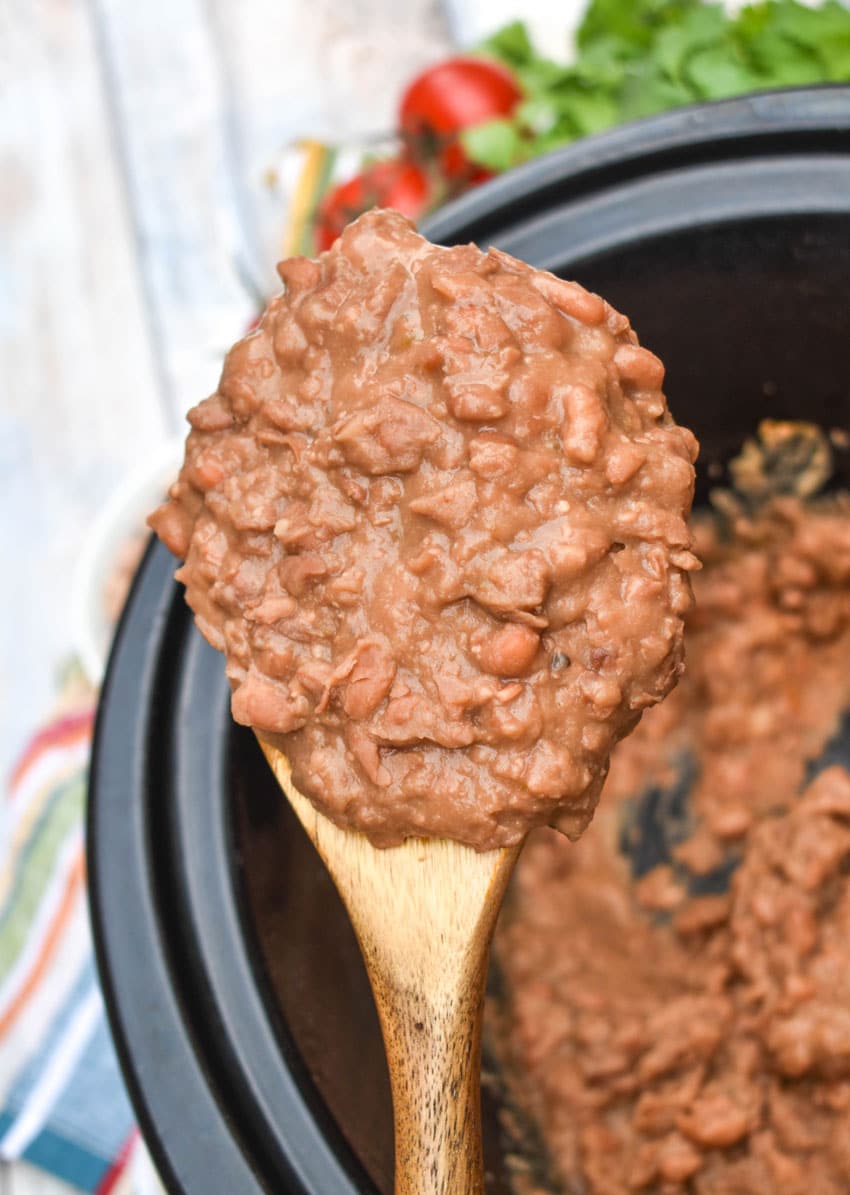a wooden spoon holding up a scoop of homemade refried beans
