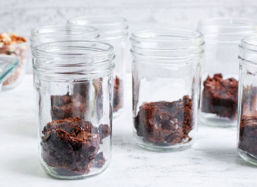 torn up chunks of baked brownies in the bottom of small glass jars