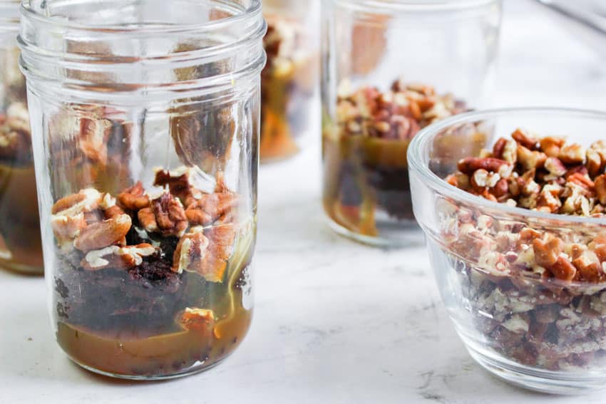 layers of brownie bits, caramel syrup, and chopped pecans in small glass jars