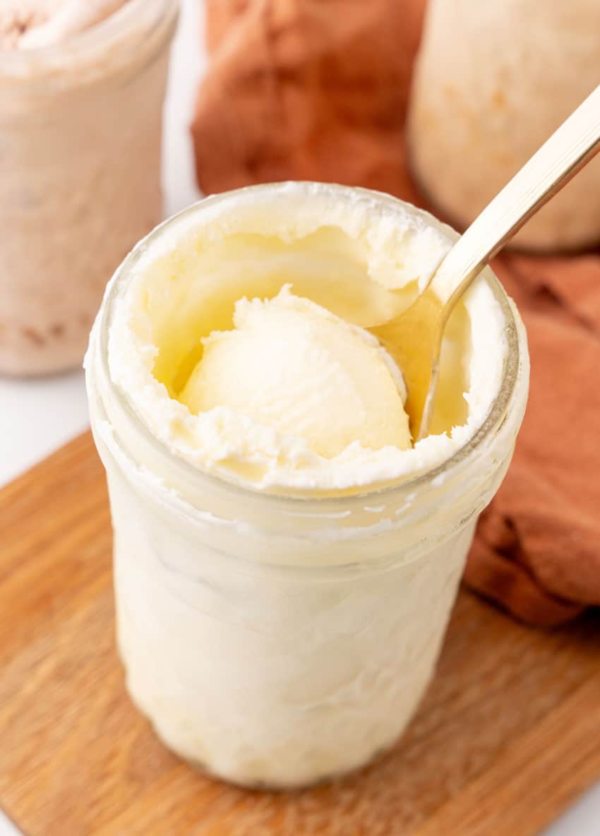 a spoon scooping homemade vanilla ice cream out of a glass mason jar