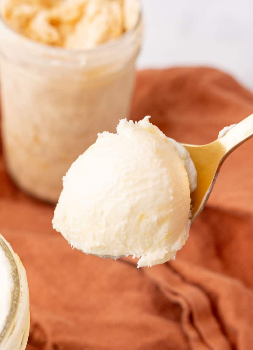 a spoon holding up a scoop of homemade creamy mason jar ice cream