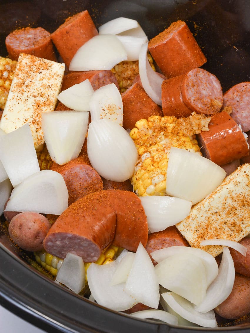seasoned sausage, onions, corn and potatoes in the bowl of a slow cooker