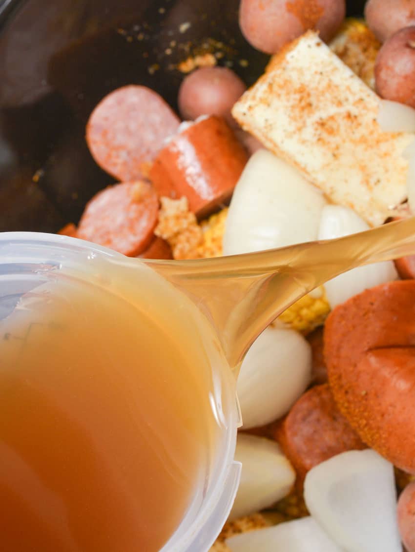 chicken broth being poured into the black bowl of a slow cooker