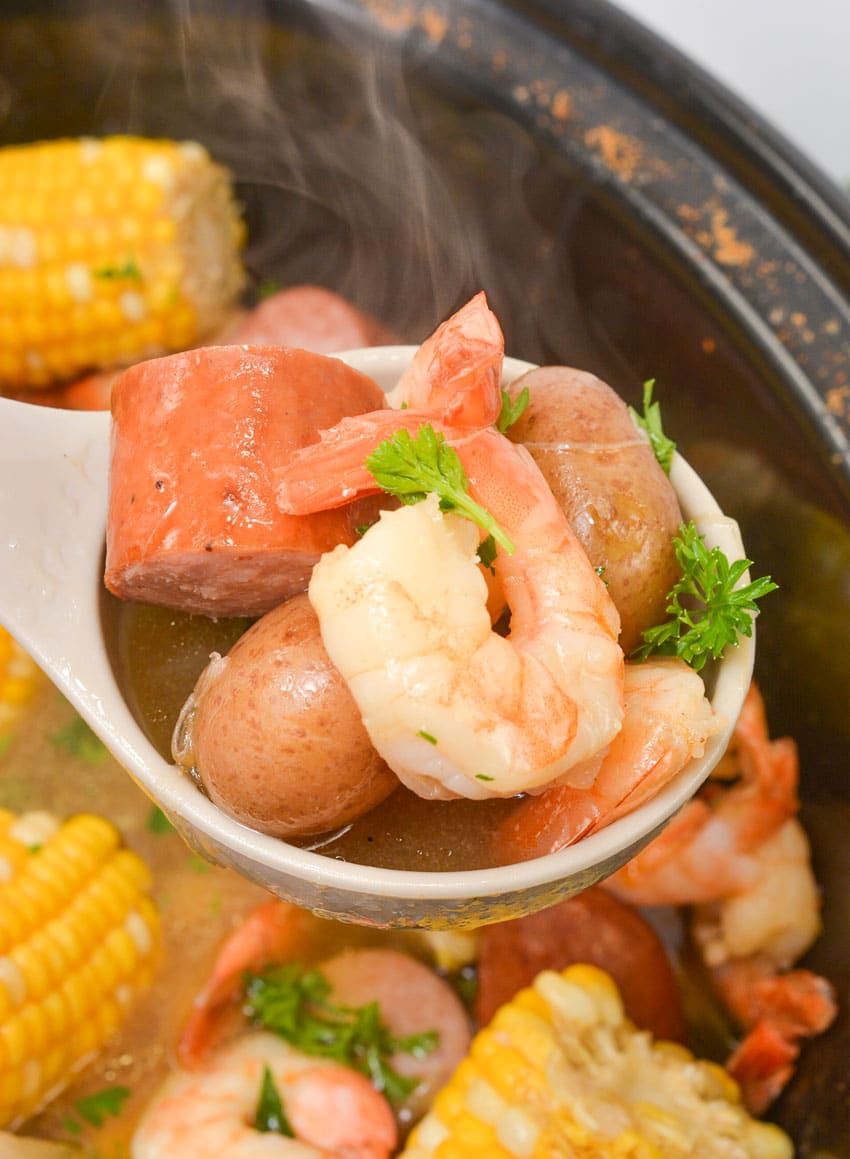 a white ladle holding up a scoop of a crockpot shrimp boil