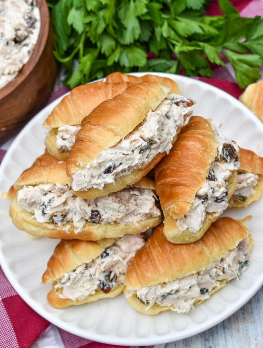 creamy tarragon chicken salad stuffed mini croissants stacked on a small white plate