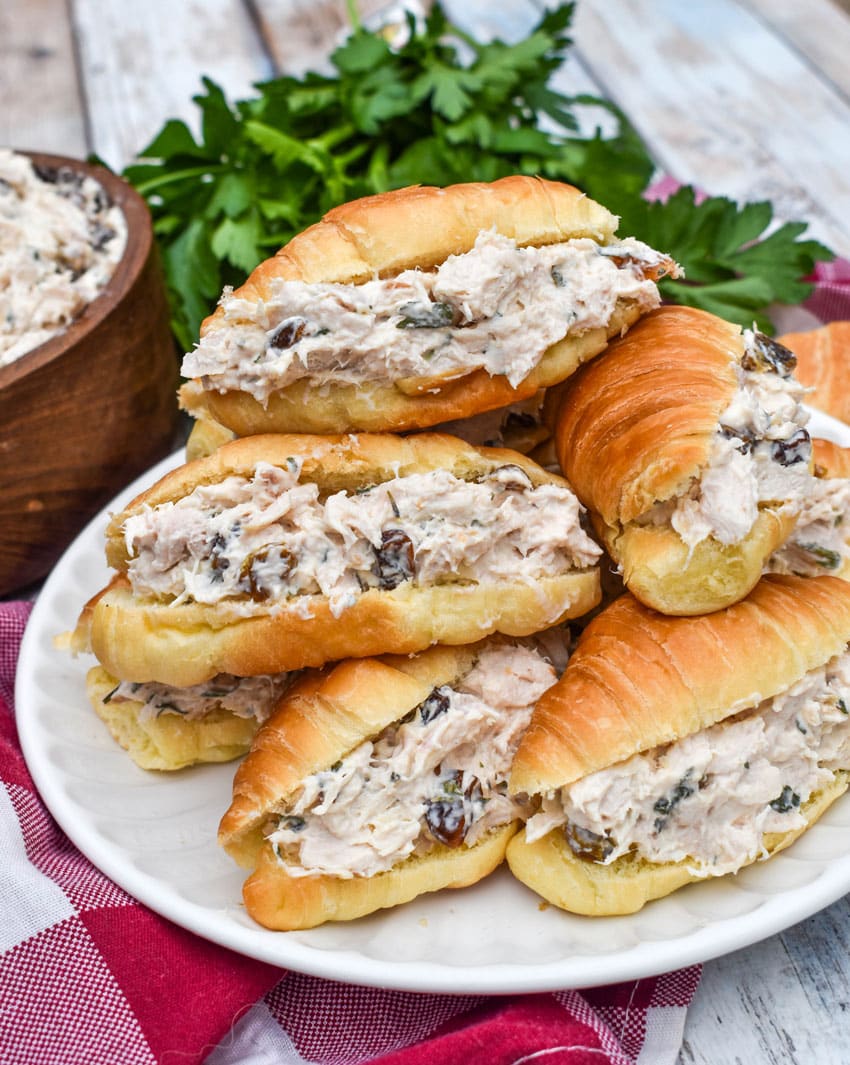creamy tarragon chicken salad stuffed mini croissants stacked on a small white plate