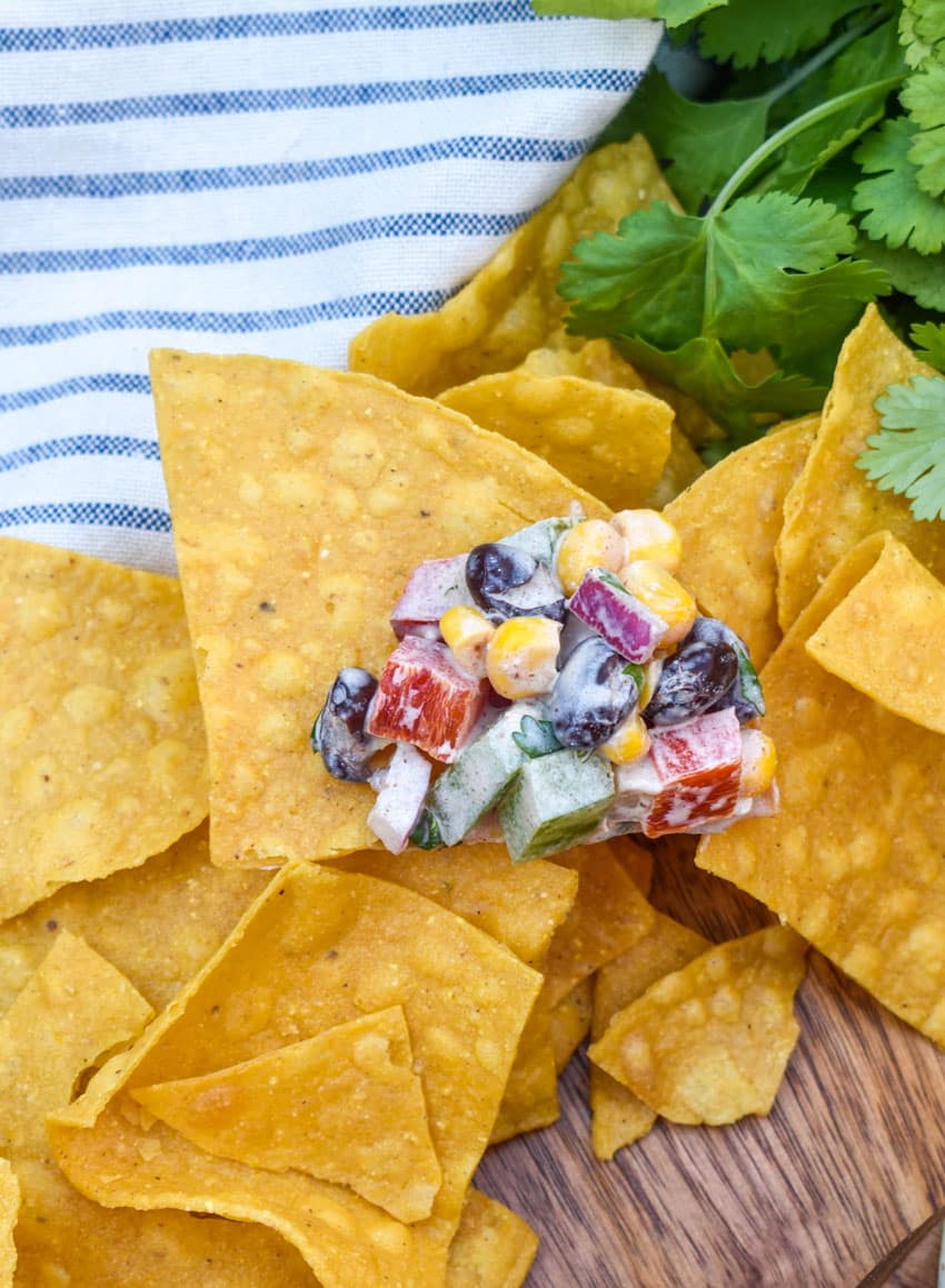 a tortilla chip topped with creamy black bean salsa resting on a pile of chips on a wooden cutting board