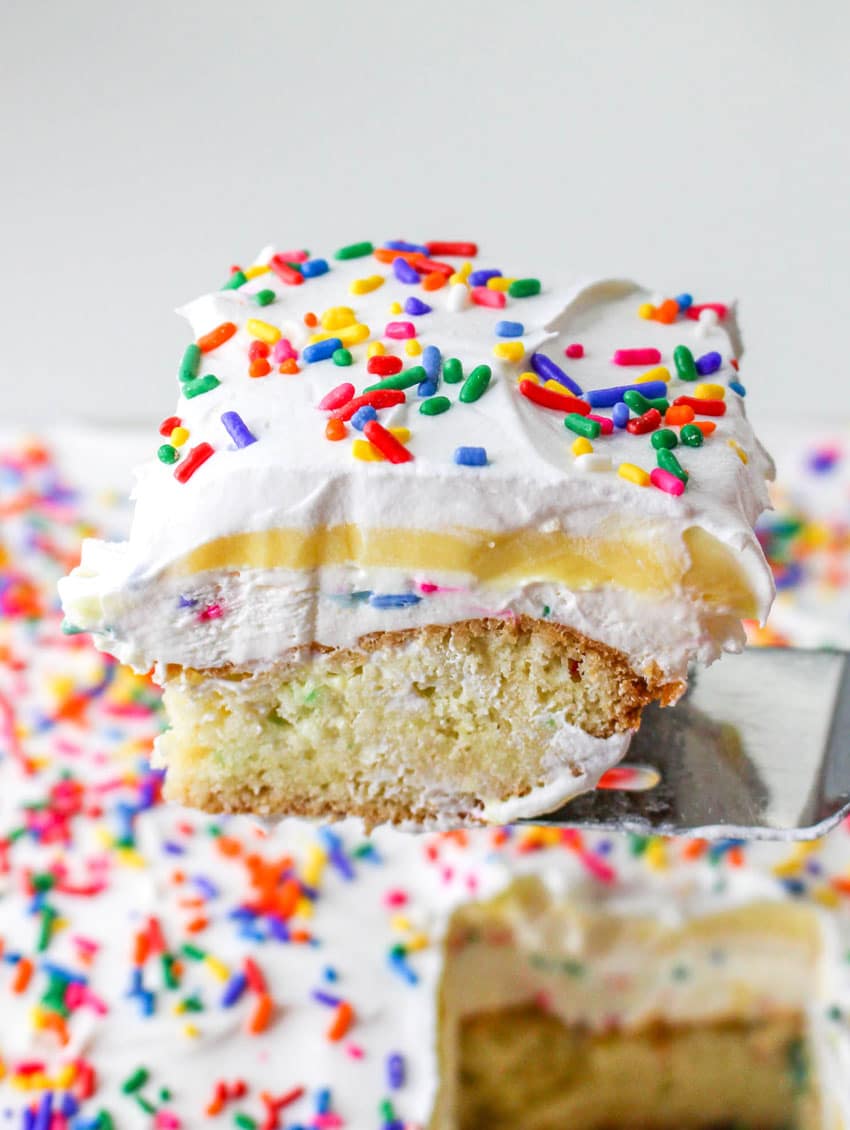 a silver spatula holding up a slice of a layered funfetti dessert cake