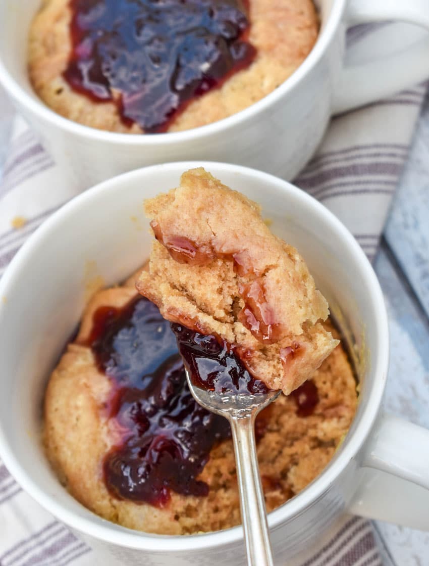 a silver fork holding up a scoop of a peanut butter mug cake topped with grape jelly