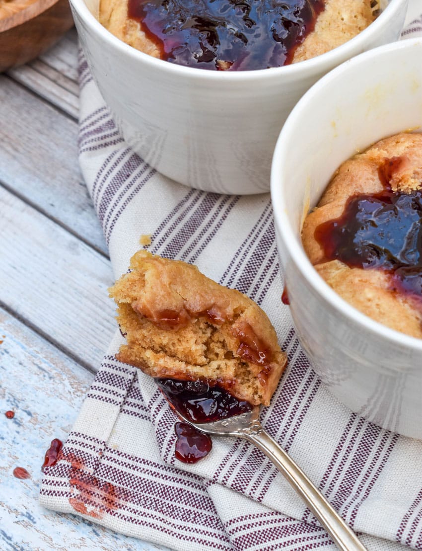 a silver fork holding a scoop of a peanut butter mug cake topped with grape jelly resting on a wooden table