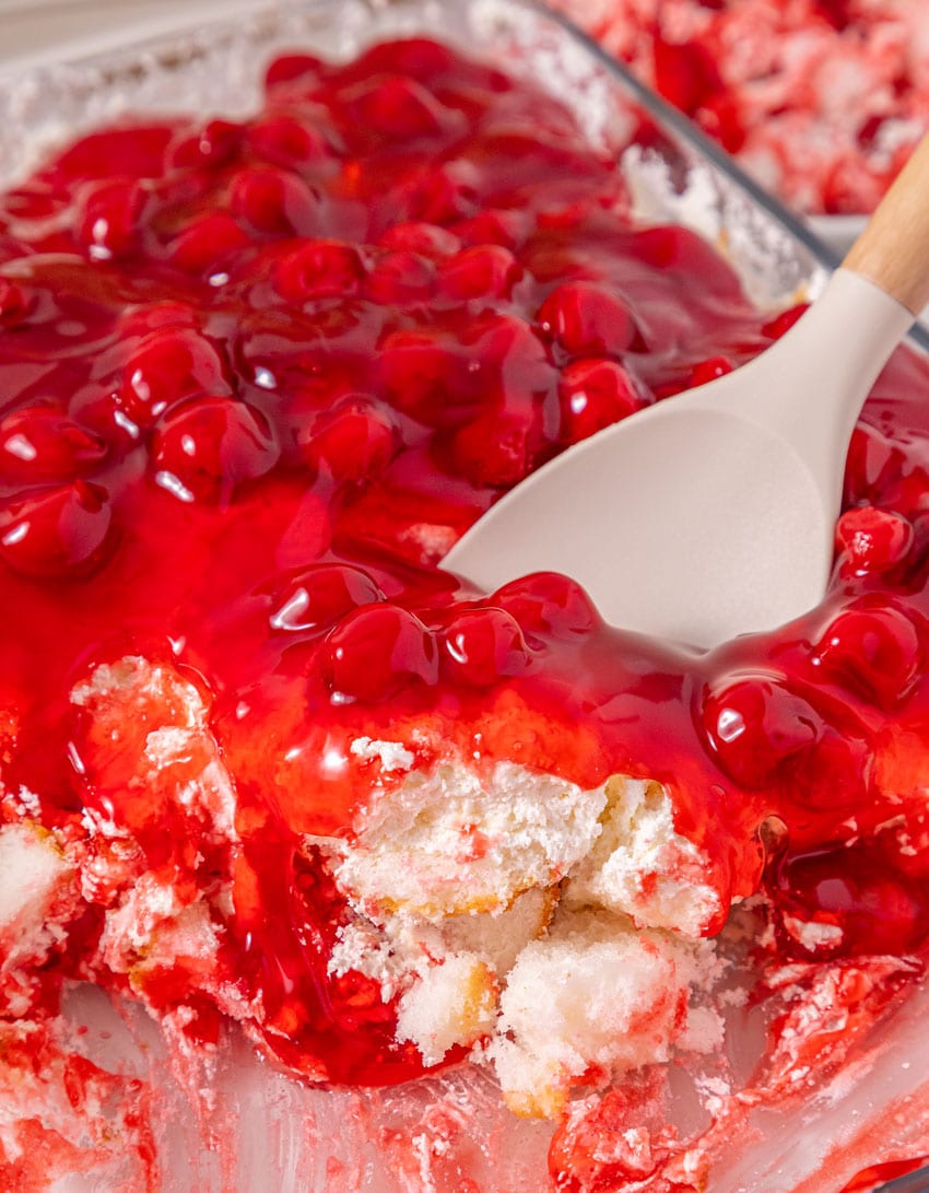a wooden handled spoon scooping old fashioned cherries in the snow dessert out of an aluminum pan