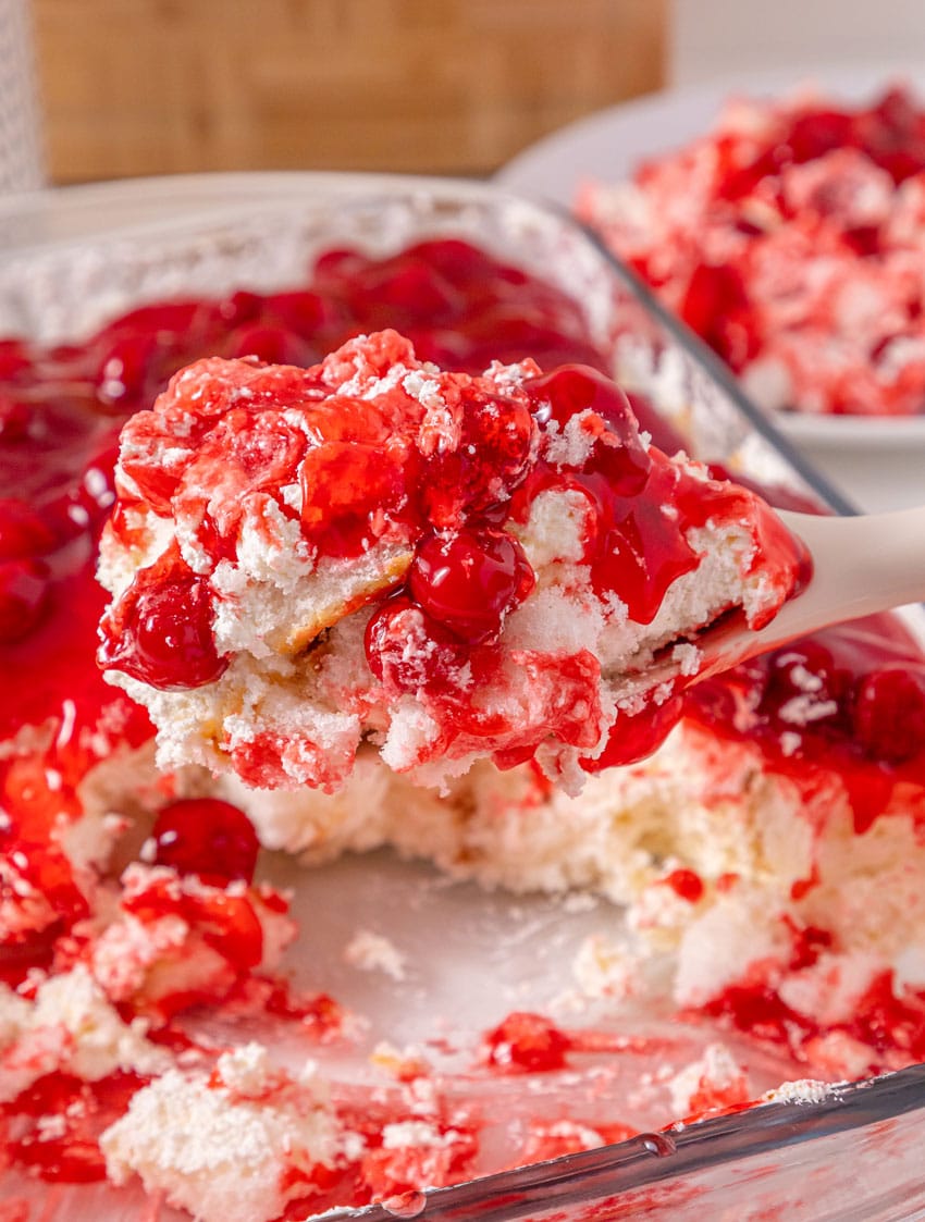 a serving spoon holding up a scoop of a layered no bake cherries in the snow dessert