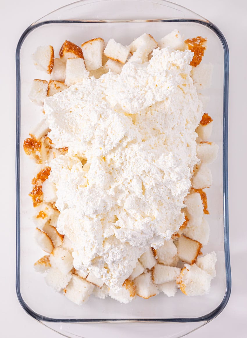 whipped cream cheese spread over angel food cake pieces in a glass baking dish