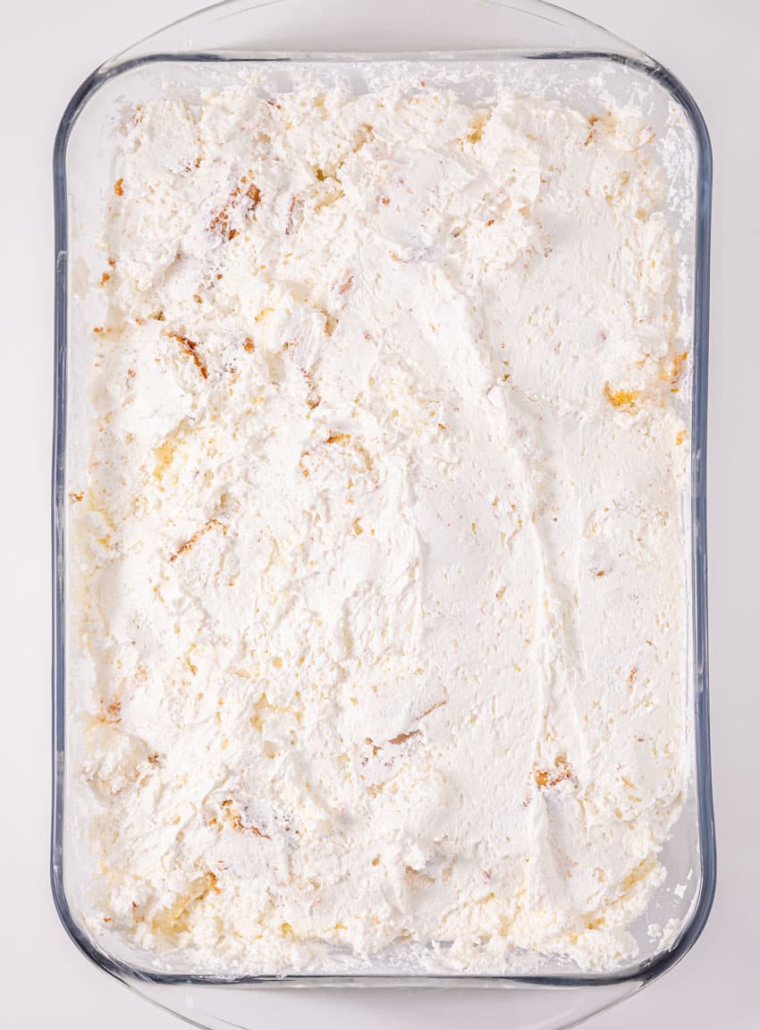 whipped cream cheese spread over angel food cake pieces in a glass baking dish