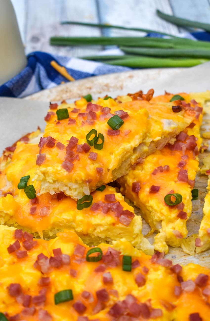slices of breakfast pizza with hashbrown crust on a parchment paper lined pizza pan