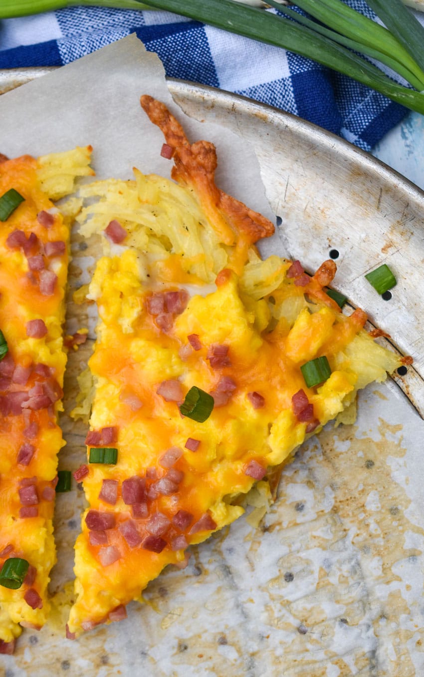 slices of breakfast pizza with hashbrown crust on a parchment paper lined pizza pan