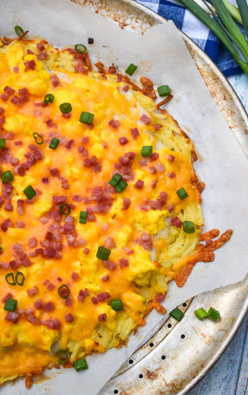 a breakfast pizza with a hashbrown crust on a parchment paper lined pizza pan