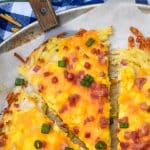 slices of breakfast pizza with hashbrown crust on a parchment paper lined pizza pan