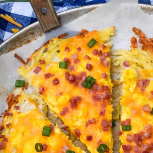 slices of breakfast pizza with hashbrown crust on a parchment paper lined pizza pan