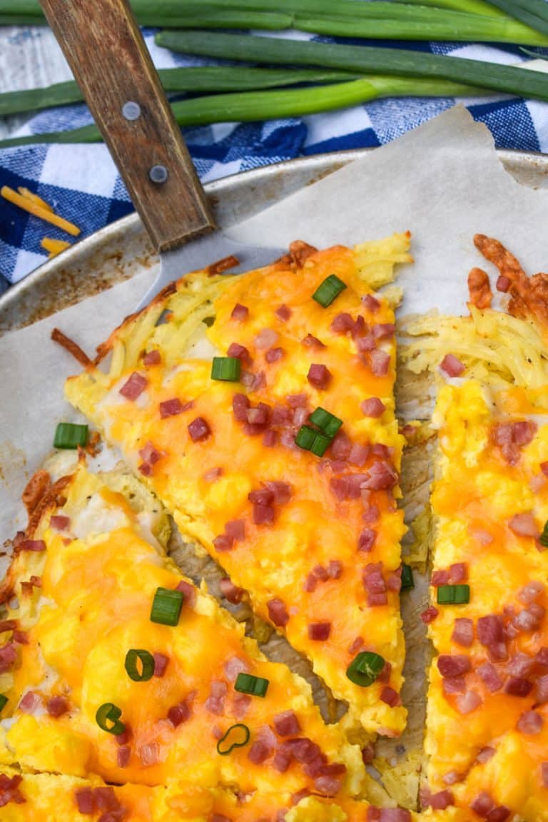 slices of breakfast pizza with hashbrown crust on a parchment paper lined pizza pan