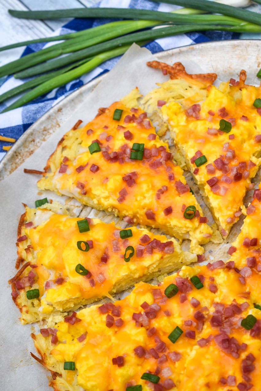 slices of breakfast pizza with hashbrown crust on a parchment paper lined pizza pan
