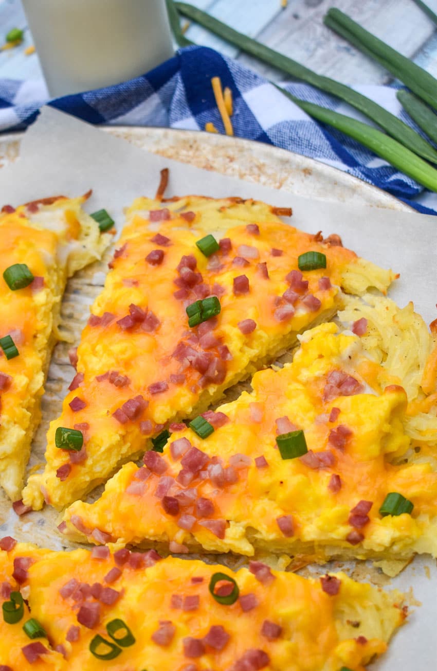 slices of breakfast pizza with a hashbrown crust on a parchment paper lined pizza pan