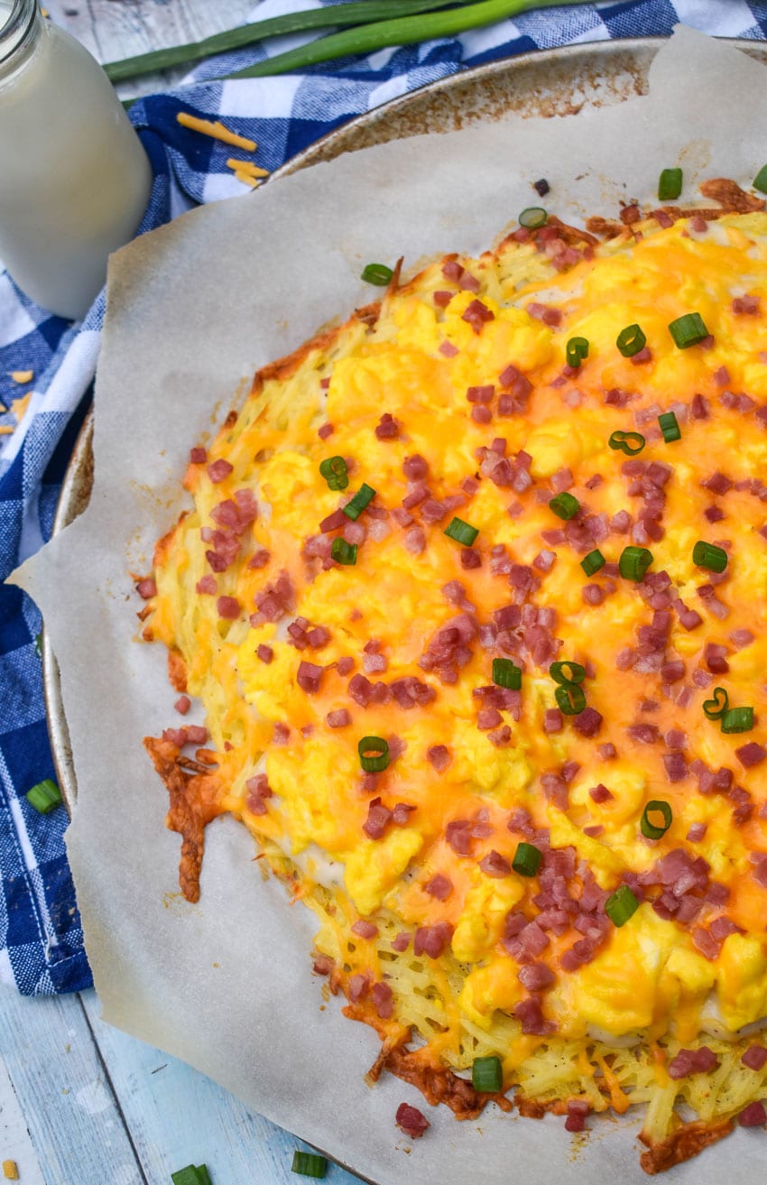 a breakfast pizza with a hashbrown crust on a parchment paper lined pizza pan