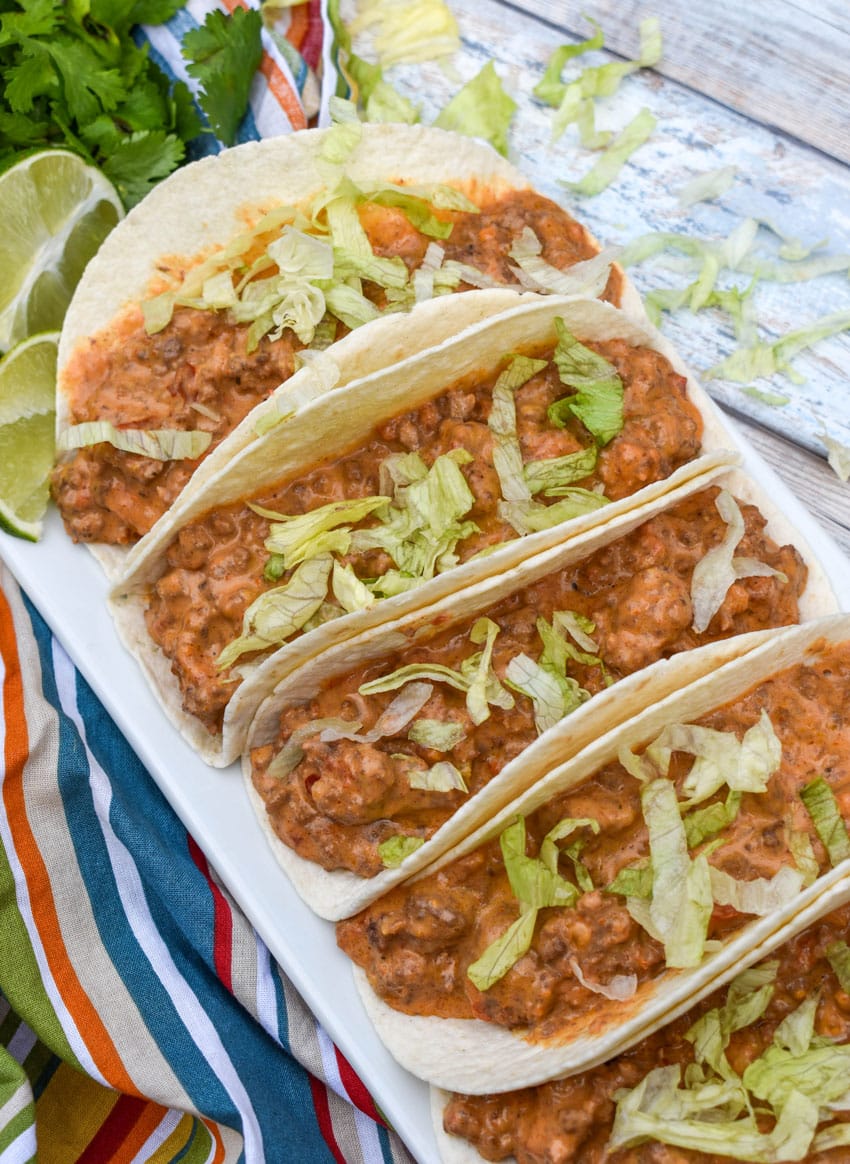 cheesy rotel beef soft tacos arranged in a row on a white serving platter