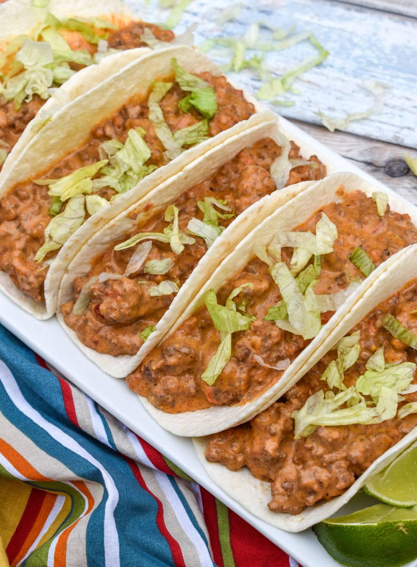 cheesy rotel beef soft tacos arranged in a row on a white serving platter