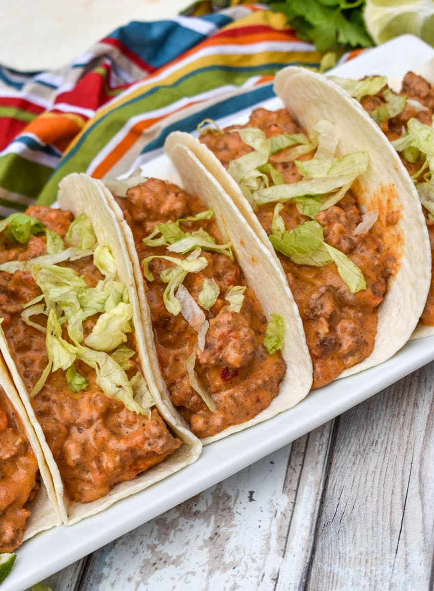 cheesy rotel beef soft tacos arranged in a row on a white serving platter