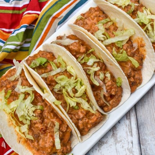 cheesy rotel beef soft tacos arranged in a row on a white serving platter
