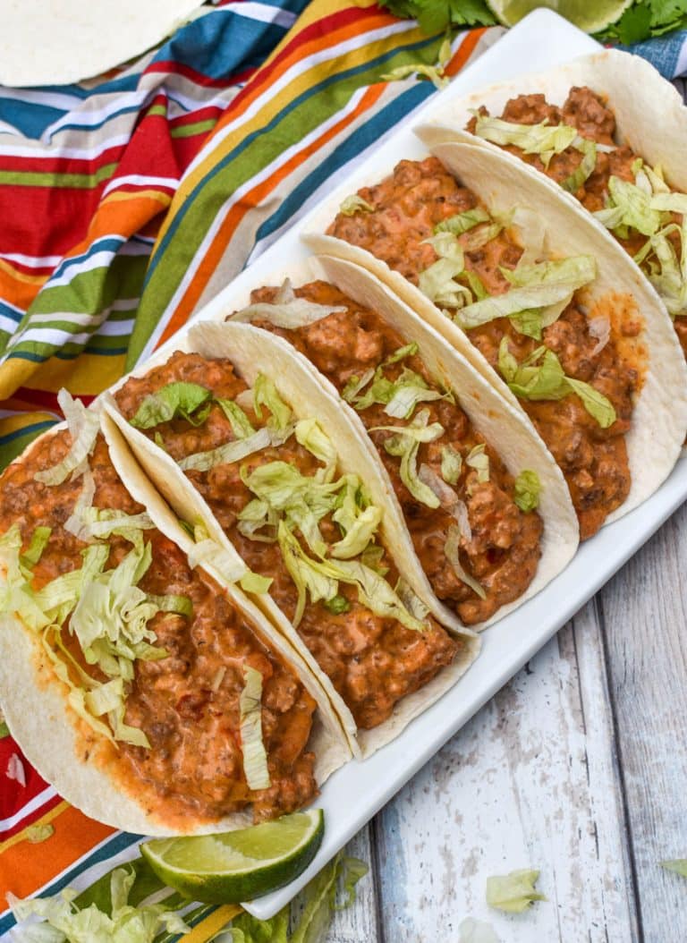 cheesy rotel beef soft tacos arranged in a row on a white serving platter