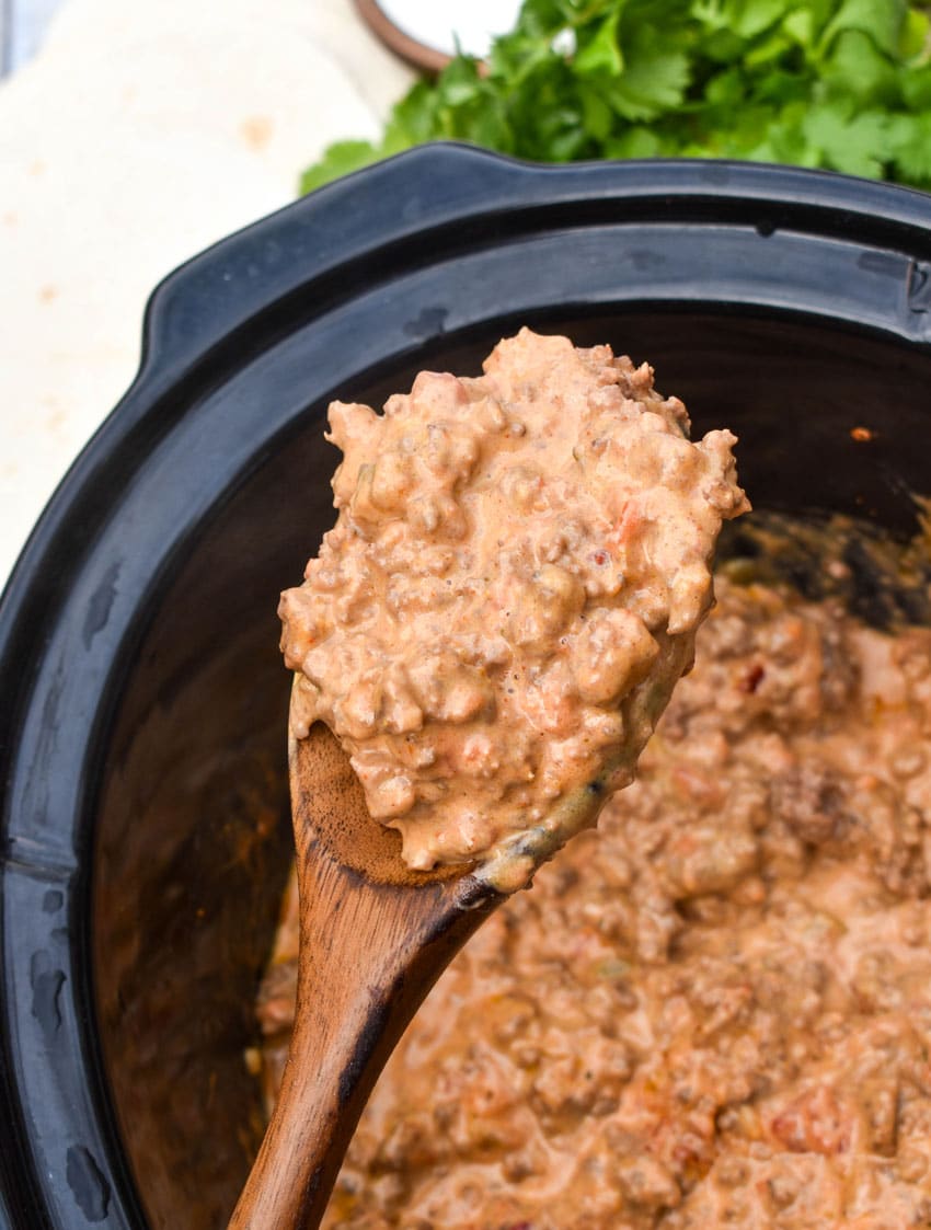 a wooden spoon holding up a scoop of cheesy rotel beef taco meat