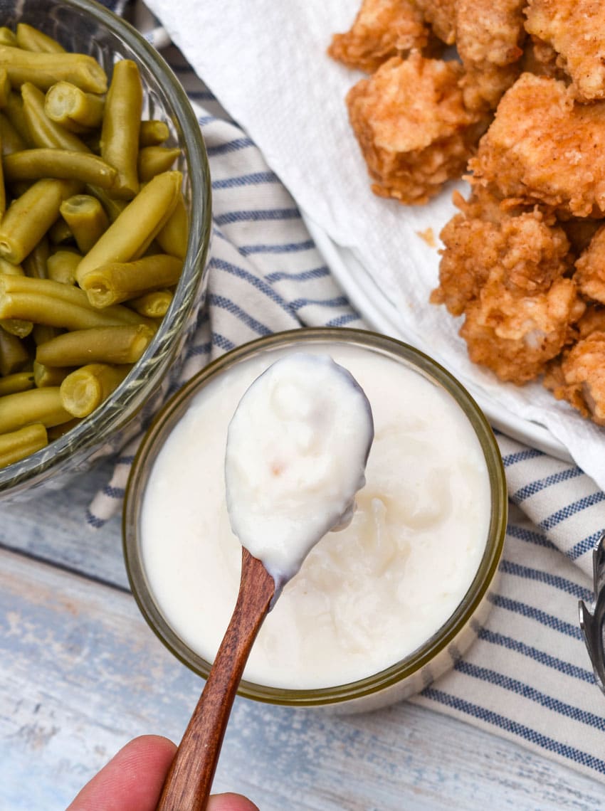 a wooden spoon holding up a scoop of homemade white country gravy