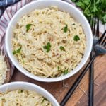 garlic parmesan ramen noodles in two white bowls resting on a wooden cutting board