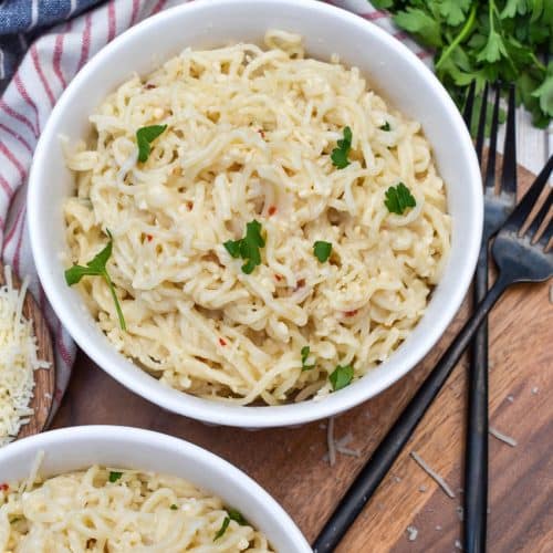 garlic parmesan ramen noodles in two white bowls resting on a wooden cutting board