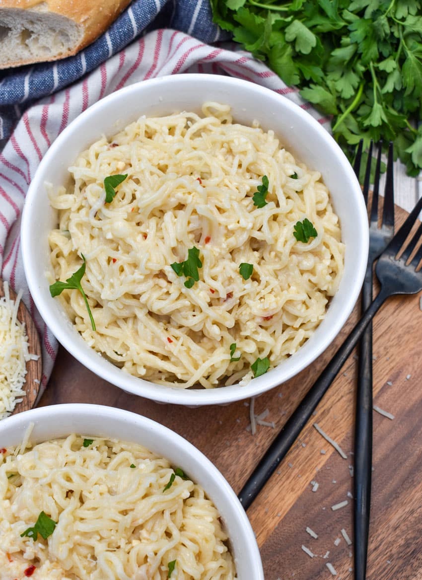 garlic parmesan ramen noodles in two white bowls resting on a wooden cutting board