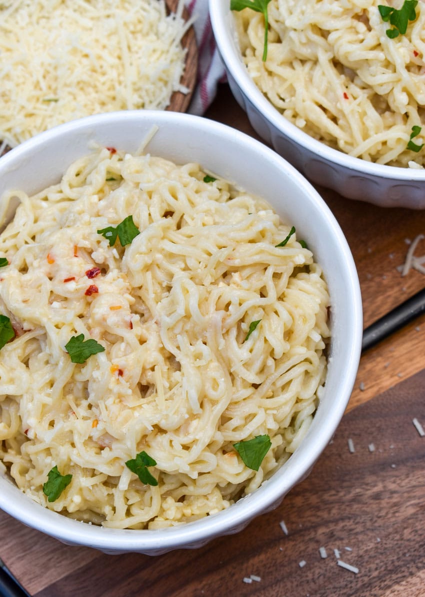 garlic parmesan ramen noodles in two white bowls resting on a wooden cutting board