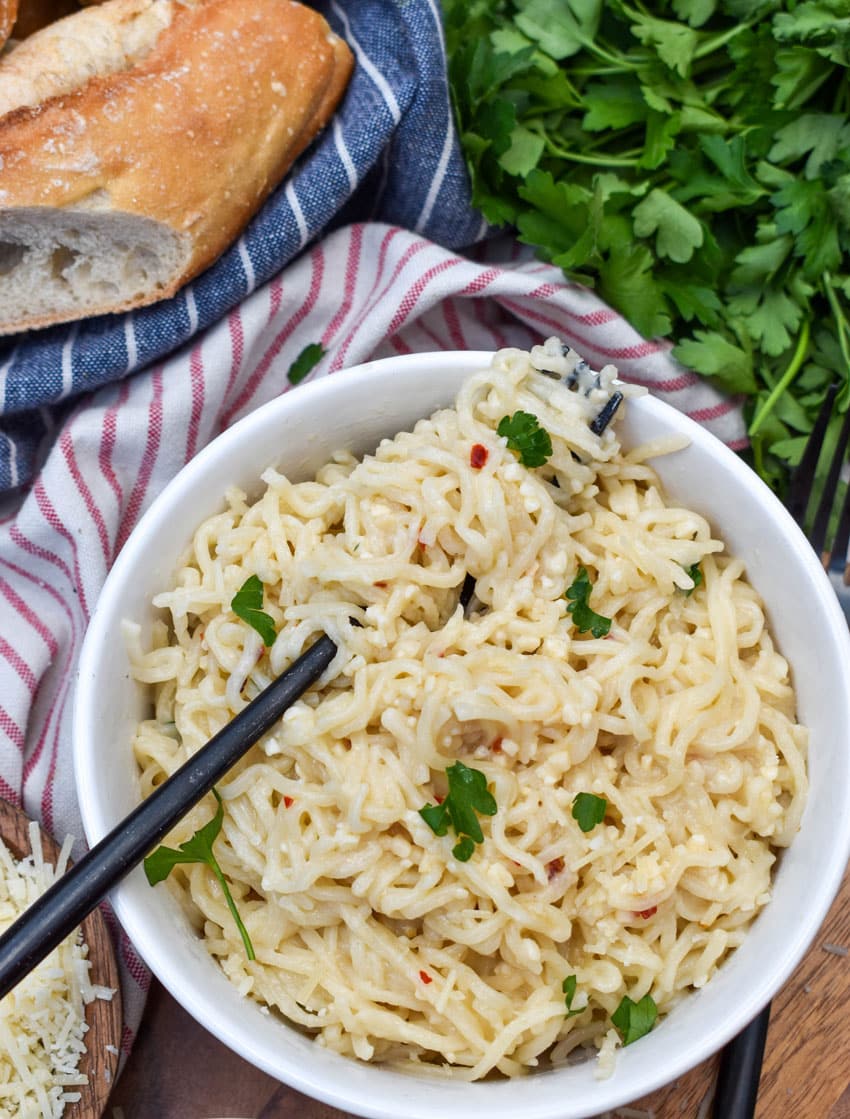 garlic parmesan ramen noodles in two white bowls resting on a wooden cutting board