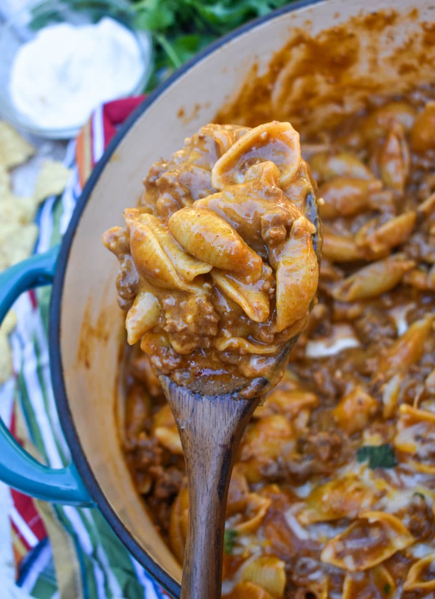 a wooden spoon holding up a scoop of homemade cheesy enchilada hamburger helper pasta