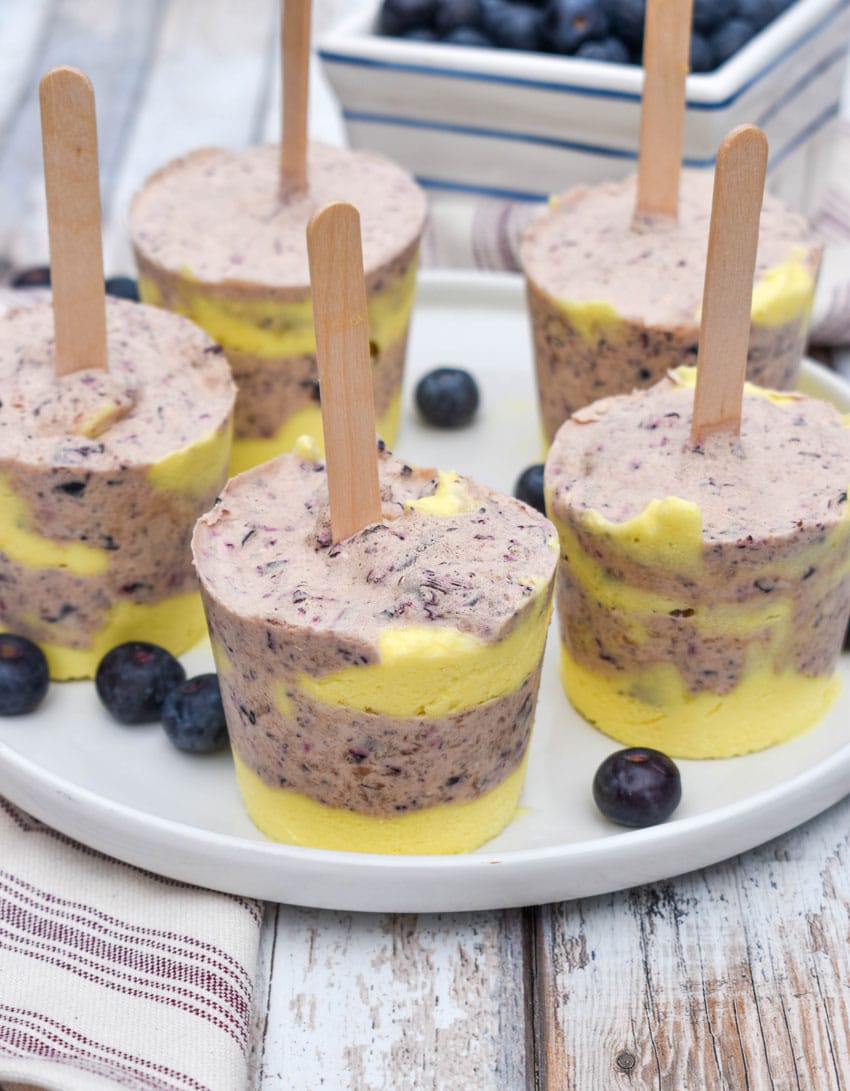lemon blueberry pudding pops on a white plate with fresh blueberries on the side