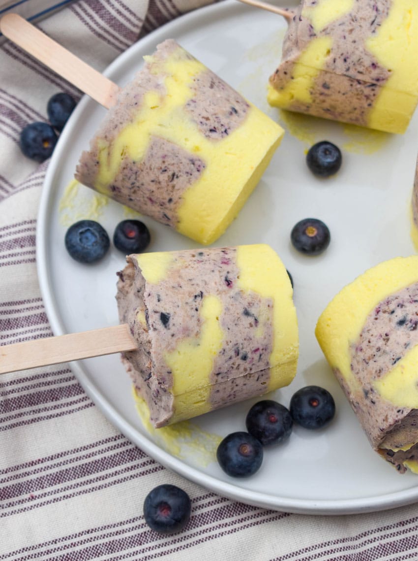 lemon blueberry pudding pops on a white plate with fresh blueberries on the side