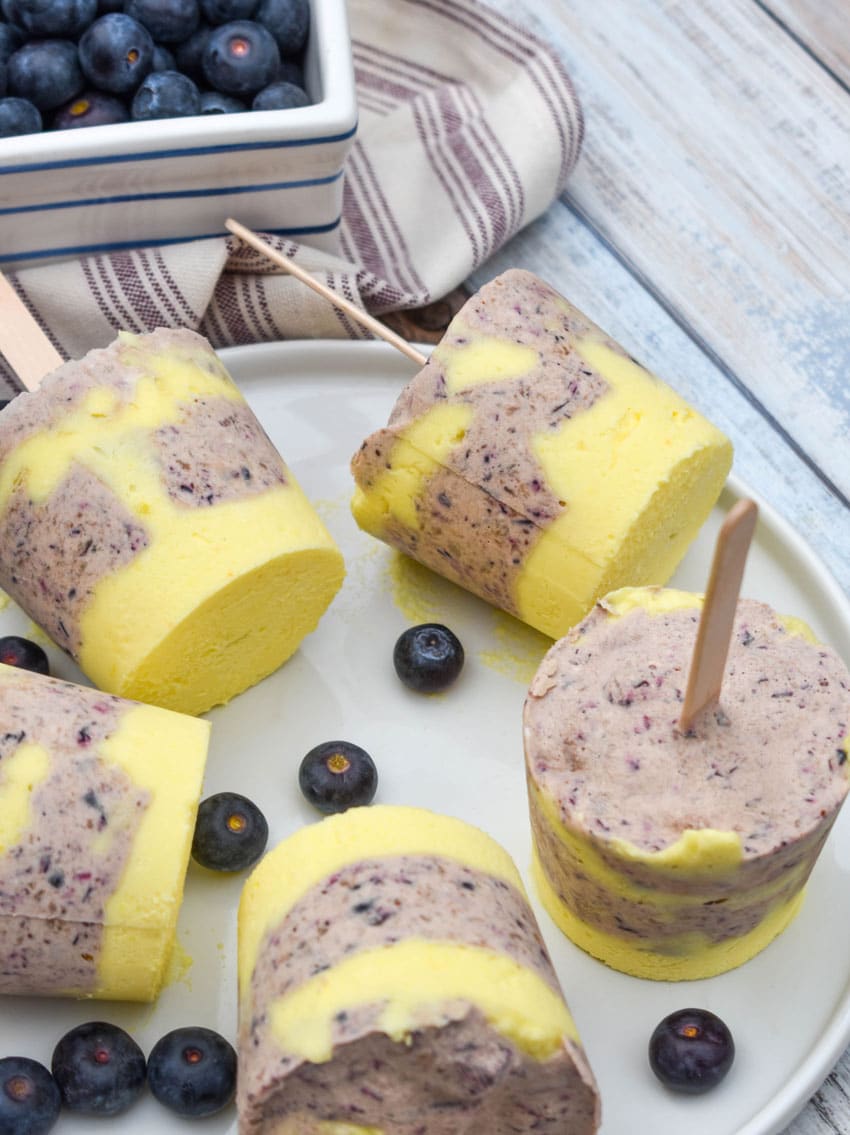 lemon blueberry pudding pops on a white plate with fresh blueberries on the side