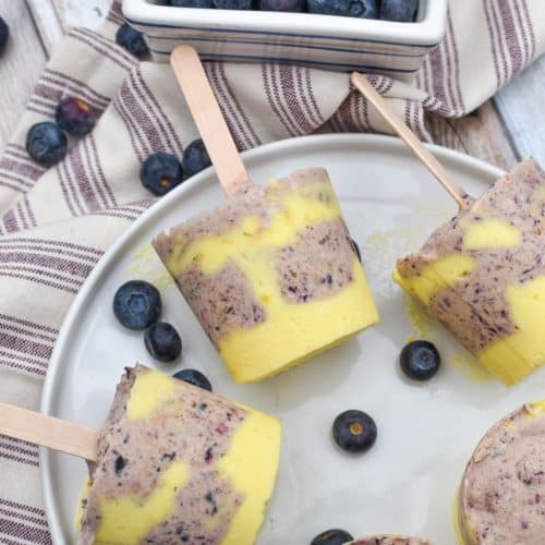 lemon blueberry pudding pops on a white plate with fresh blueberries on the side